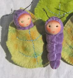 two small dolls are laying on a green and yellow leaf shaped piece of cloth with thread