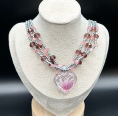 This piece is a graceful, layered heart shaped Andara Crystal necklace and sea bead necklace. The center heart piece has beautiful pink swirls. The colors are absolutely stunning. Colors are light pink to a pleasing purple and grey. This necklace is adjustable. Also, this necklace is lightweight and can be worn all day with ease. Will you add this to your collection? Will not be made again. Pink Necklaces With Heart Charm For Jewelry Making, Pink Beaded Necklace With Heart Pendant As Gift, Pink Double Strand Necklace For Gift, Handmade Pink Heart Crystal Necklaces, Pink Heart Pendant Beaded Necklace For Gift, Pink Heart Pendant Beaded Necklace As Gift, Pink Heart Pendant Beaded Necklace For Valentine's Day, Pink Heart Beads Pendant Necklace, Pink Multi-strand Jewelry Gift