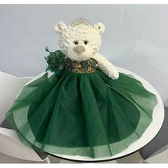 a white teddy bear wearing a green tutu skirt and tiara on top of a table