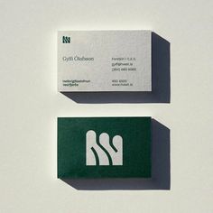 two business cards sitting side by side on top of a white surface with green lettering