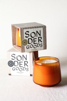 an orange candle sitting in front of a box with the words sonder goods on it