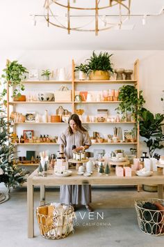 a woman standing in front of a table filled with potted plants and other items