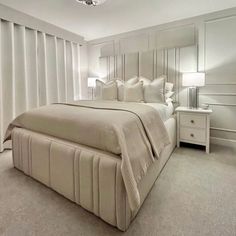 a large bed sitting in the middle of a bedroom next to a window with white curtains