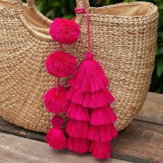 a straw bag with pink tassels hanging from it's side on a wooden table