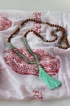 this 108 bead mala is designed by here & there creative and handmade in northern india with sandalwood and lava stone beads. the beads originate from the spiritual lands of northern india and have been blessed by the holy ganges river.  green jade is said to be a symbol of tranquility, purity, peace, and harmony.  here & there styling tip: if the tassel strands become tangled, dip in a cup of water and hang to let dry. materials: natural sandalwood and green jade beads Dip In A Cup, Handmade Jade Necklaces For Meditation, Holistic Mala With Natural Stones For Meditation, Green Gemstone Beads Mala For Healing, Holistic Healing Mala With Wooden Beads, Green Bohemian Mala For Meditation, Holistic Natural Stones Mala For Meditation, Green Beaded Mala For Healing, Traditional Mala With Natural Stones For Meditation