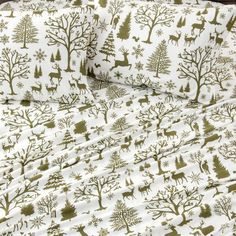 a bed covered in white and green sheets with deer, trees and snowflakes on them