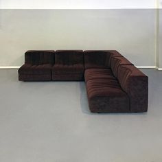 a brown sectional couch sitting on top of a floor next to a white wall in an empty room