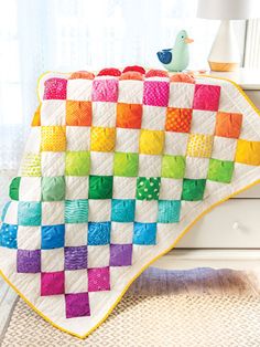 a colorful quilt on a white dresser next to a window with a bird sitting on top of it