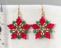 two red and green beaded earrings on a white piece of cloth next to a ruler