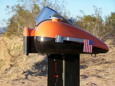 an orange motorcycle parked on top of a dirt road next to a dry grass field