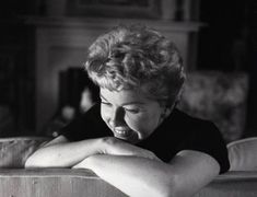 a black and white photo of a woman leaning her head on the back of a couch