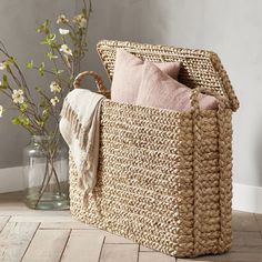 a woven basket with two pillows on the floor next to a vase filled with flowers