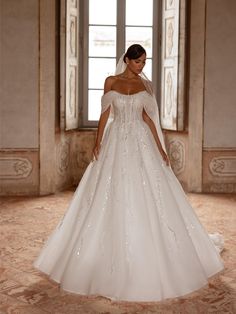 a woman in a white wedding dress standing by a window