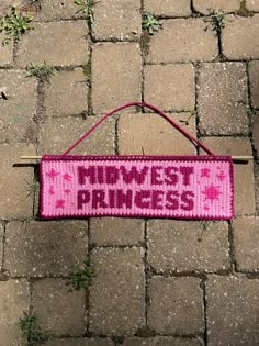 a pink knitted sign that says,'lowest princess'hanging on a brick walkway