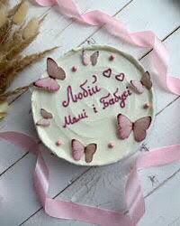 a cake with pink butterflies on it sitting next to some dried grass and ribbon tied around the edge