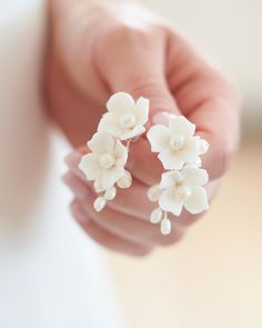 a person holding two white flowers in their hand and one is wearing earrings with pearls on them