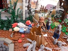 an assortment of legos are displayed on a table in front of a building with trees and bushes