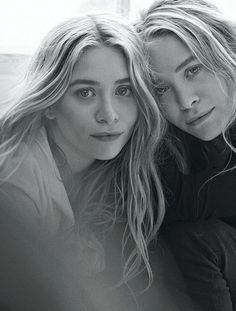 two beautiful women sitting next to each other in front of a window and looking at the camera