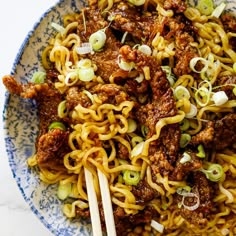 a blue and white bowl filled with noodles, meat and veggies on chopsticks