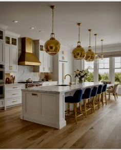 a kitchen filled with lots of white counter tops and gold pendant lights hanging from the ceiling