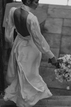 a woman in a white dress is walking down the stairs with flowers on her hand