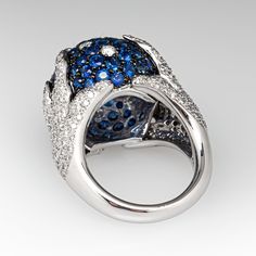 This dazzling ring is centered with a domed setting accented with seventy-eight (78), bead set, round brilliant cut natural blue sapphires and eight (8), bead set, round brilliant cut diamonds. The shank features a organic design and is accented with a total of two hundred eight (208), bead set, round brilliant cut diamonds. The ring measures 17.1mm at the top, rises 13.3mm above the finger, tapering to 3.8mm wide and 2.0mm thick at the base of the shank. The ring is size 7.5 and resizing is not recommended. Evening Diamond Ring With Gemstone, Luxury Blue Diamond Ring With Accents, Luxury Oval Sapphire Ring With Pave Setting, Luxury Sapphire Cluster Ring, Luxury Sapphire Birthstone Ring, Luxury Formal Blue Diamond Ring, Luxury Sapphire Diamond Ring With Polished Finish, Luxury Blue Sapphire Platinum Ring, Luxury Diamond Dome Ring