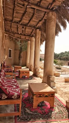 an outdoor seating area with tables and couches under a thatched roof in the desert