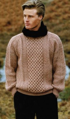 a man wearing a sweater and black pants stands in front of a field with grass