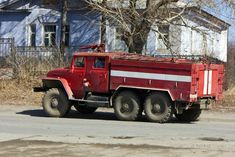 an old red truck is parked on the side of the road in front of a house