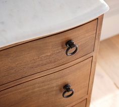 a close up of a drawer on a wooden cabinet with white marble top and black handles