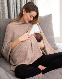 a woman holding a baby wrapped in a blanket on top of a couch next to a window