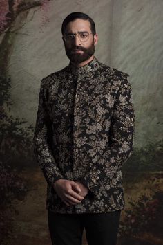 a man with a beard and glasses standing in front of a wallpapered background