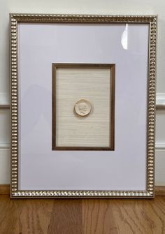 a white and gold frame with a button on the inside of it, sitting on a wooden floor