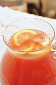 a pitcher filled with liquid sitting on top of a table next to a slice of lemon