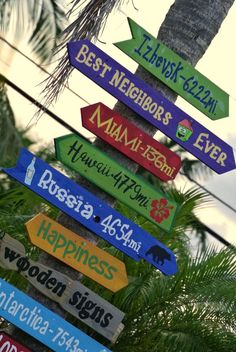 a sign post with many different colored signs on it's sides and palm trees in the background