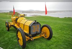 an old yellow tractor sitting in the grass near some water and red flags on a cloudy day