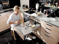 a woman sitting at a kitchen counter with food in front of her and reading a newspaper