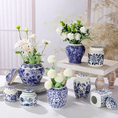 blue and white vases with flowers in them sitting on a table next to rolls of toilet paper