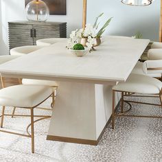 a dining room table with white chairs and flowers on the centerpiece, in front of a mirror