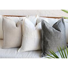 three pillows sitting on top of a white couch next to a potted plant in front of a wall