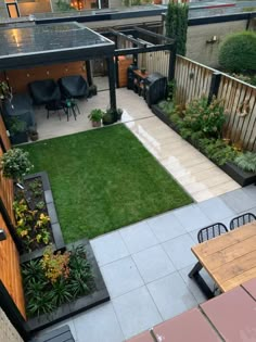 an outdoor patio with grass and wooden tables in the center, surrounded by small garden areas