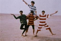 four young men are posing on the beach for a photo with their arms in the air