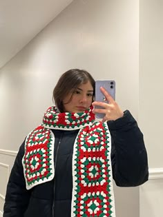 a woman taking a selfie while wearing a crocheted scarf and holding a cell phone