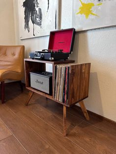 a record player sitting on top of a wooden table next to a chair and painting