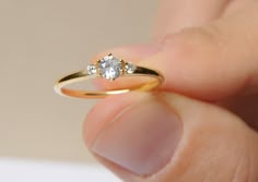 a woman's hand holding a gold ring with two diamonds on it and one diamond in the middle