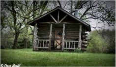 an old log cabin sits in the middle of a field