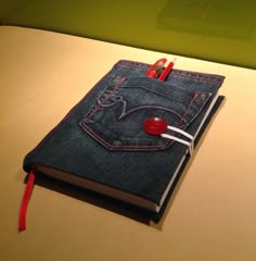 an open notebook with a red button on the front and blue denim pocket, sitting on top of a table