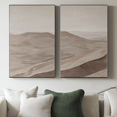 two paintings hang on the wall above a couch in a room with white walls and green pillows