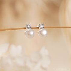 a pair of white pearl and diamond earrings sitting on a twig in front of a blurry background