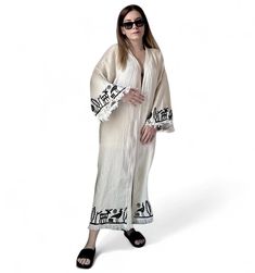 The Hittite printed  muslin kimono combines elegance and comfort seamlessly. Made from organic cotton, it offers an eco-friendly choice, while the OEKO-TEX certification ensures its health and environmental consciousness.  The kimono will elevate every moment with its sophistication, featuring unique patterns created using traditional woodblock printing and natural dyes. Suitable for both casual and special occasions, it effortlessly complements various outfits, adding a touch of style to your l Cream Kaftan For Spring Vacation, Spring Vacation Cream Kaftan, Traditional Maxi Dress With Kimono Sleeves For Festival, Traditional Printed Kimono For Beach Cover-up, Spring Folk Long Kimono, Beige Kimono Sleeve Dress For Beach, Beige Dress With Kimono Sleeves For Beach, White Maxi Dress With Kimono Sleeves For Summer, White Bohemian Beach Robe